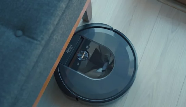 Black iRobot robot vacuum poking out from underneath a grey sofa