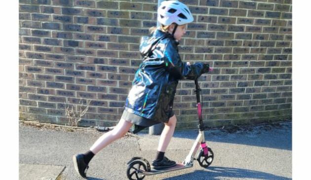 A primary school aged girl in a white helmet riding a pink and black scooter