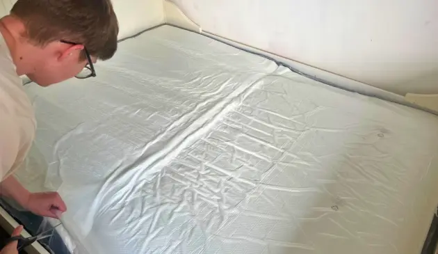 Poppy cutting the outer plastic wrapping from the Panda Hybrid Bamboo Mattress Pro on a bed