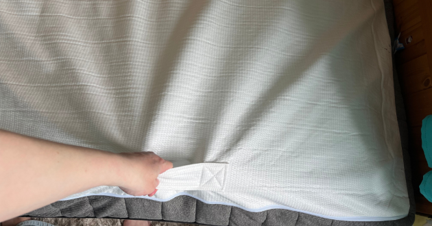 Hand lifting the removable white top cover of the Panda Hybrid Bamboo Mattress beside its side handle and zip