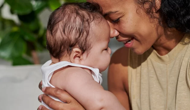 A woman holds her baby to her face in the sunshine