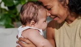 A woman holds her baby to her face in the sunshine