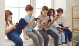 Five children sat on a windowsill using their smartphones