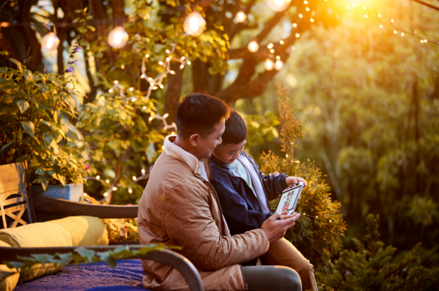 A father and son playing on a Nintendo Switch outside in the garden together