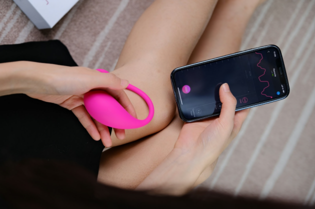 A woman holding a pink sex toy and her phone looking at her toy's usage
