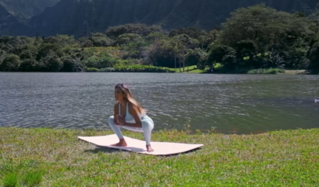 A woman doing Kegel squat holds on the grass near water