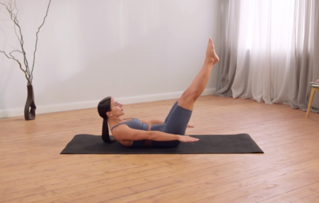 A woman performs Pilates move The Hundred on a yoga mat in her living room