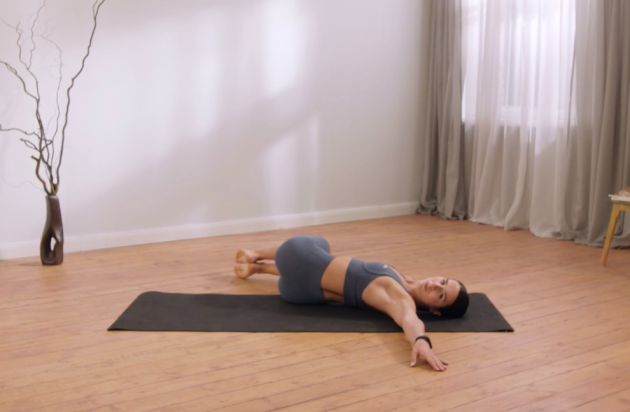 A woman performs Spinal twists on her yoga mat in her living room
