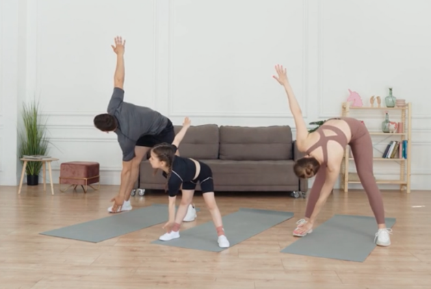 A family of three doing Windmill exercises together on yoga mats at home