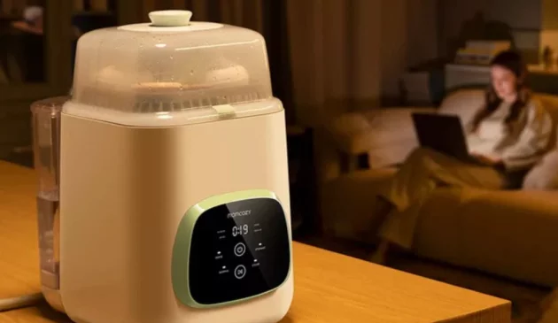 An image of the Momcozy KleanPal Pro washer and steriliser on a table while a mother works