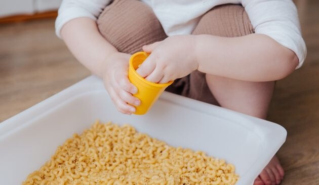 Baby playing with pasta and cup