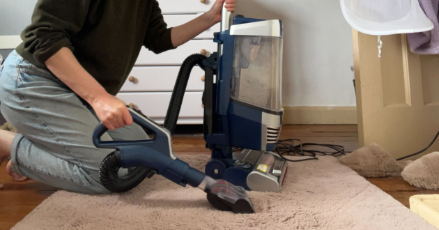 a woman using the hose attachment of a shark stratos xl vacuum cleaner to vacuum a rug