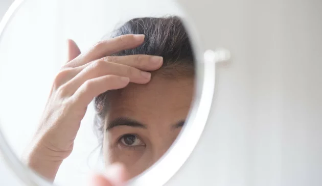 A woman examines her hair in a circle mirror