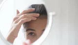 A woman examines her hair in a circle mirror