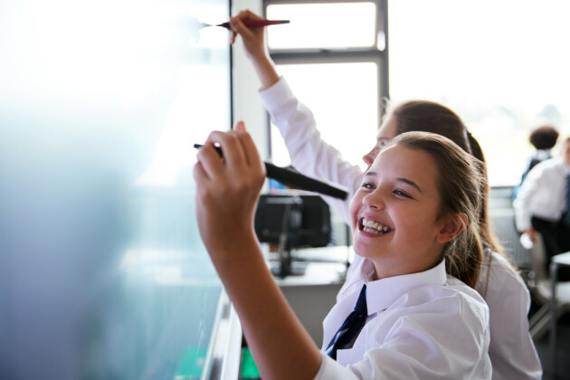A happy school student is drawing on an interactive whiteboard, she's smiling
