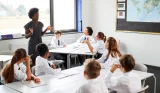A teacher is stood up speaking to a room of students at school
