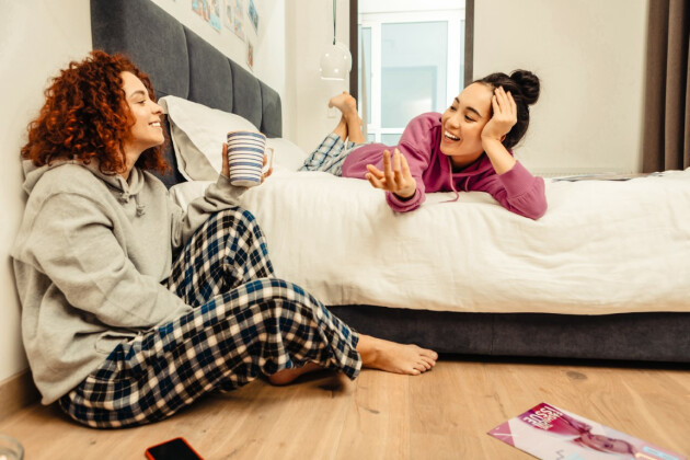 Two female roommates talking in their comfy clothes, one on the floor and one on the bed