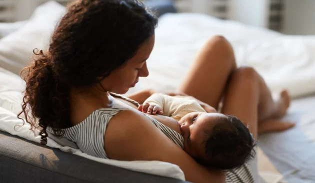 Mother breastfeeding newborn baby while lying comfortably on bed in peaceful bedroom setting with natural light