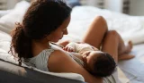 Mother breastfeeding newborn baby while lying comfortably on bed in peaceful bedroom setting with natural light