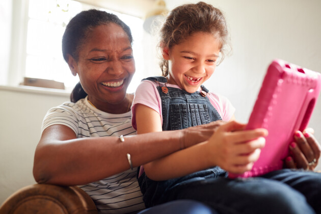 A mother and child laughing together while looking at a pink tablet