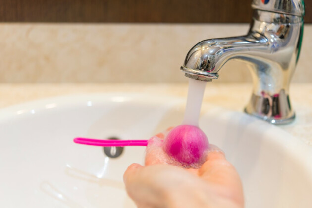 A hand washes a ben wa ball under water from a tap