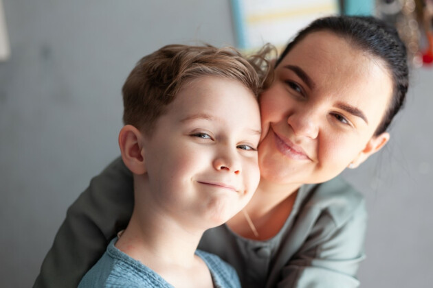A mother wither her son are hugging, while the son is looking at the camera smiling