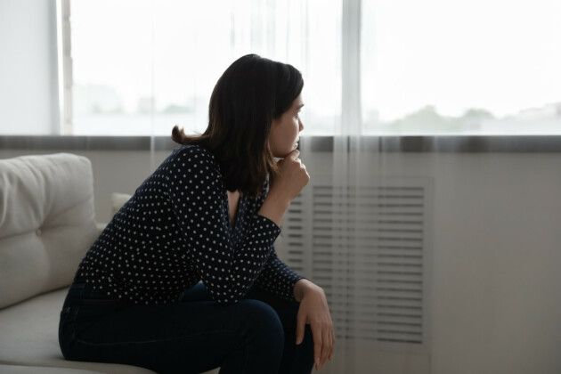 A woman looks longingly out of the window, she appears sad and in deep thought