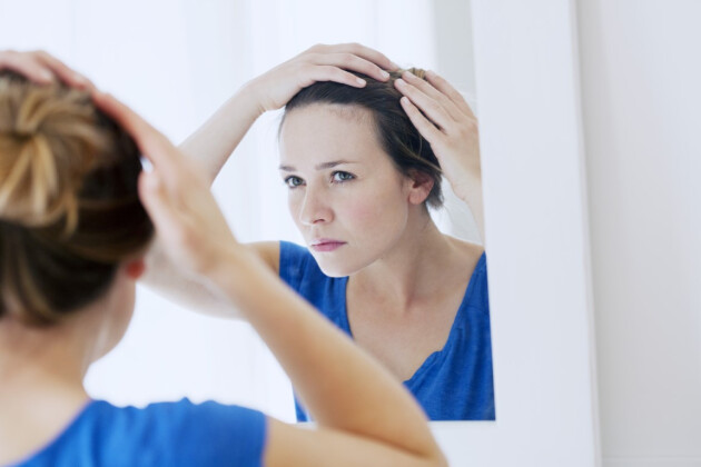 A woman inspects her hair in a mirror
