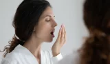 A woman holds her mouth up to smell her breath