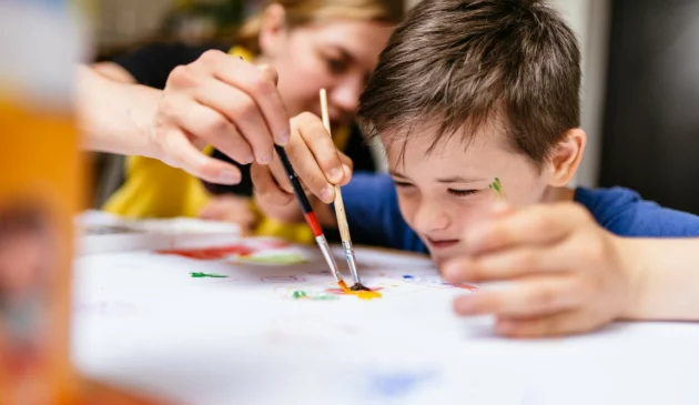A young boy with autism is painting with a teacher next to him