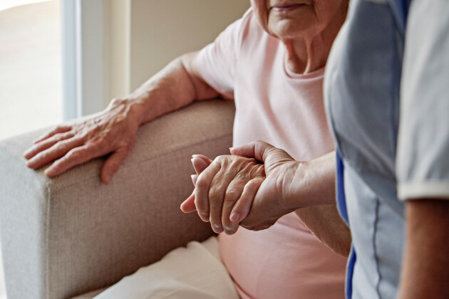 A young woman helps an elderly woman stand from a chair