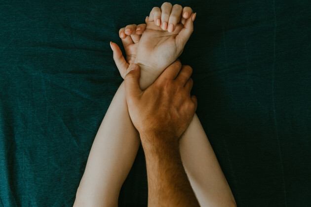 A couple's embrace hands while on top of a green bedsheet