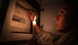 A woman checking her fuse box in candlelight