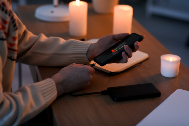 A woman attempting to charge her phone using a power bank during a power cut surrounded by candles