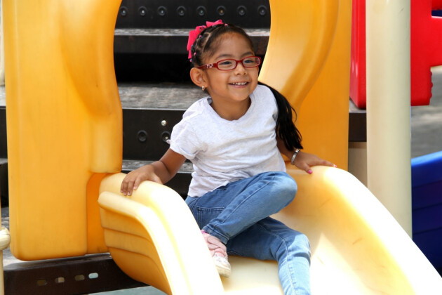 A young girl is at the top of a slide at a playground, she's smiling into the distance