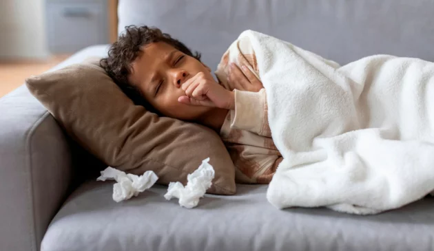 A child is sick on the sofa as he coughs into his hand
