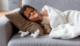 A child is sick on the sofa as he coughs into his hand