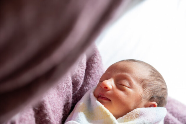 Peaceful newborn baby sleeping wrapped in soft pink blanket with natural window light in nursery room setting