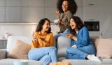 Three female friends laughing at a phone sat on the sofa together
