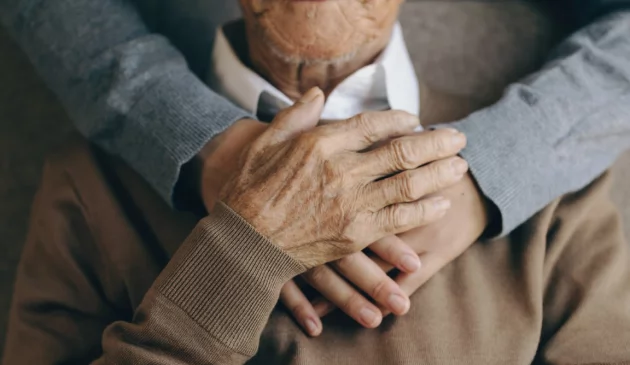 A daughter wraps her arms around her elderly father's shoulders
