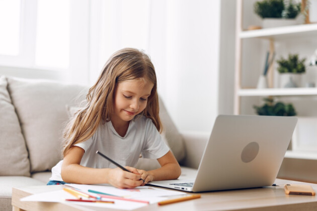 A young girl is doing homework on her laptop at home