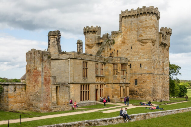 A view of people sat on the grass outside Belsay Hall Castle and Gardens, Belsay, Northumberland