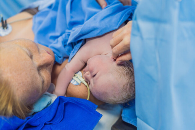 Newborn baby skin-to-skin contact with mother immediately after birth in hospital delivery room with medical staff