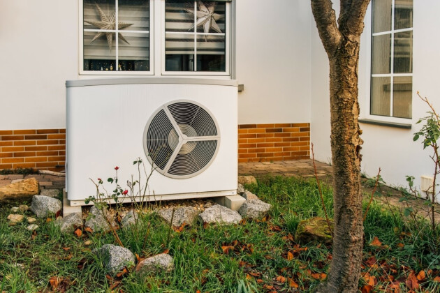 A white heat pump is sat in the corner of a UK home garden