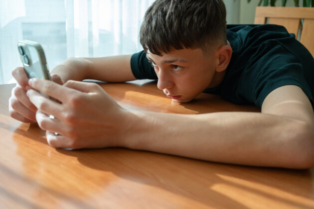 A teenager uses his phone on the dining table at home