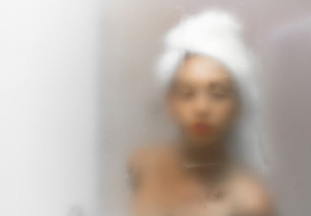 A woman with a head towel on looking into a misty mirror after a shower