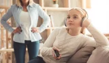 A teenager daughter with headphones on ignores her mother in the background