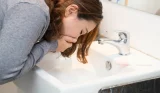 A woman has nausea and is leaning over the sink