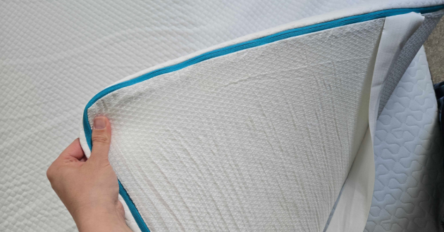 A hand shows the corner of the Simba Cool Foam Mattress Topper