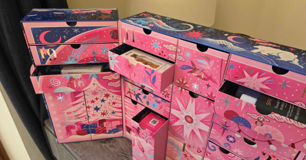 Close-up of several pink calendar drawers pulled open, with beauty products visible inside